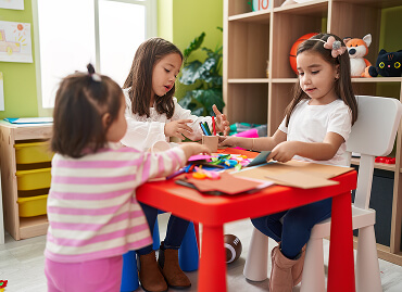 A child passing a snack to a friend at the nursery table